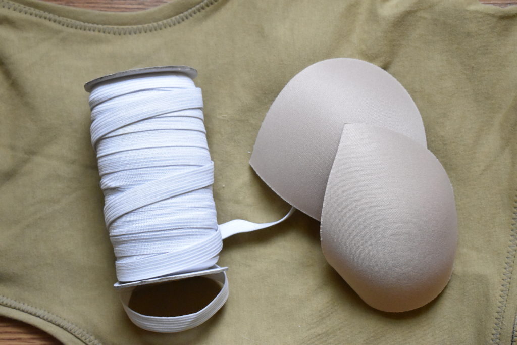 White knit elastic and two light nude coloured bra cups on top of a gold-green Axis tank.