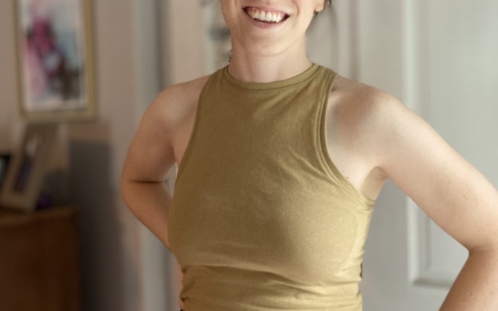 A front view of Alyssa in a gold-green Axis tank, smiling and looking at the camera with her hands on her hips