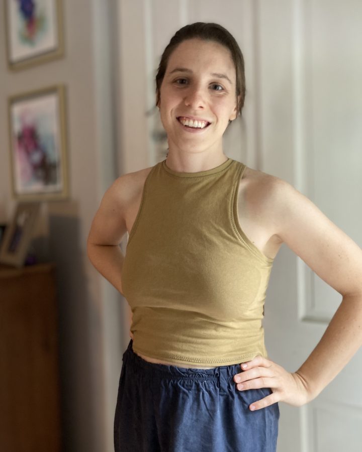 A front view of Alyssa in a gold-green Axis tank, smiling and looking at the camera with her hands on her hips